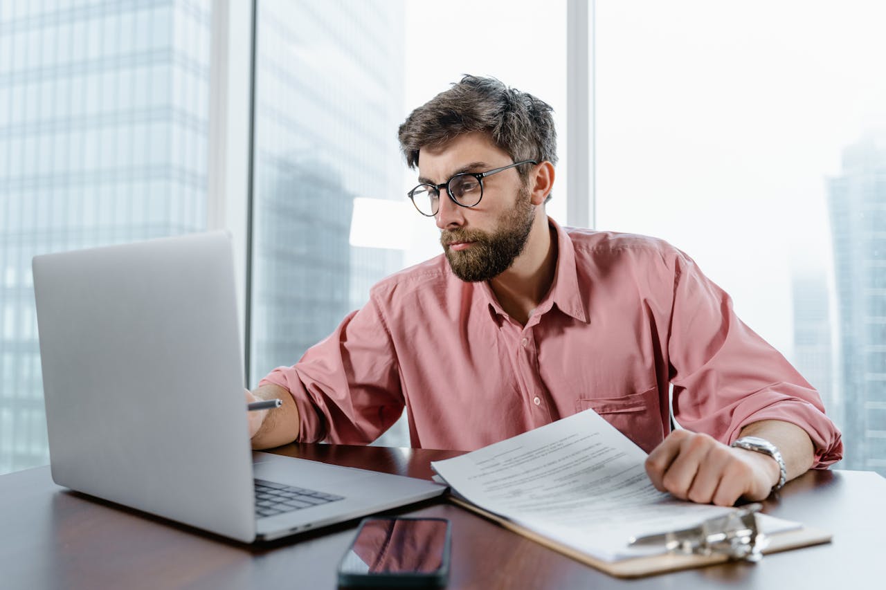 about-us A businessman in an office reviews documents and data on a laptop, concentrating on financial analysis.